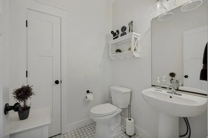 White two-panel door, pedestal sink, wall-mounted mirror, overhead lighting fixture, and hexagonal floor tiling