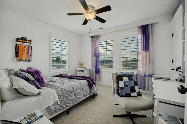 Recessed lighting, ceiling fan with light fixture, two windows with plantation shutters, light-toned carpet flooring, and white walls