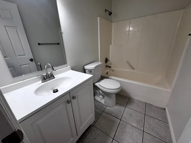 Bathroom featuring a white vanity with integrated sink, chrome faucet, wall-mounted mirror, and a combination tub/shower with a light-toned surround