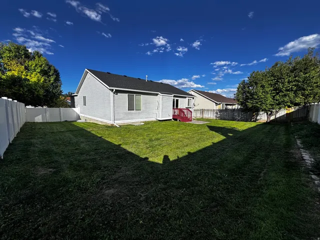 Expansive backyard featuring a manicured lawn, full privacy fencing, and a red-stained deck
