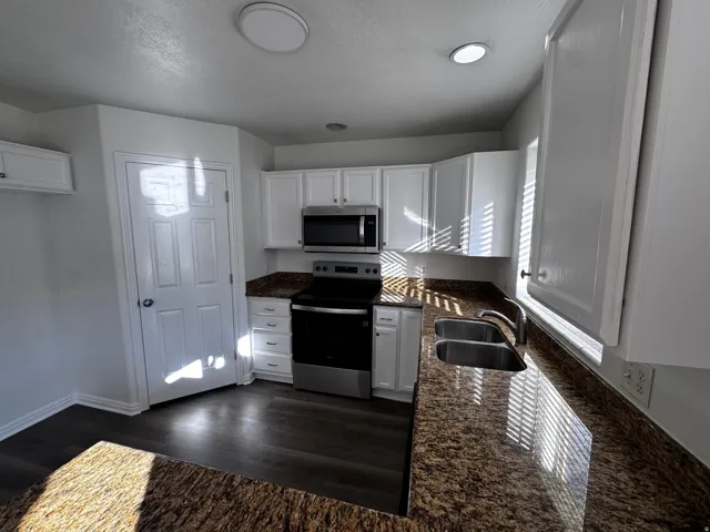 White cabinetry, stainless steel appliances, dual basin sink, and wood-finish flooring