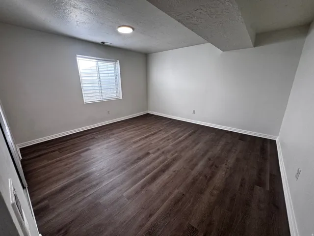Spacious room featuring wood-finish flooring, light neutral wall tones, a window with blinds, and a flush-mount ceiling light
