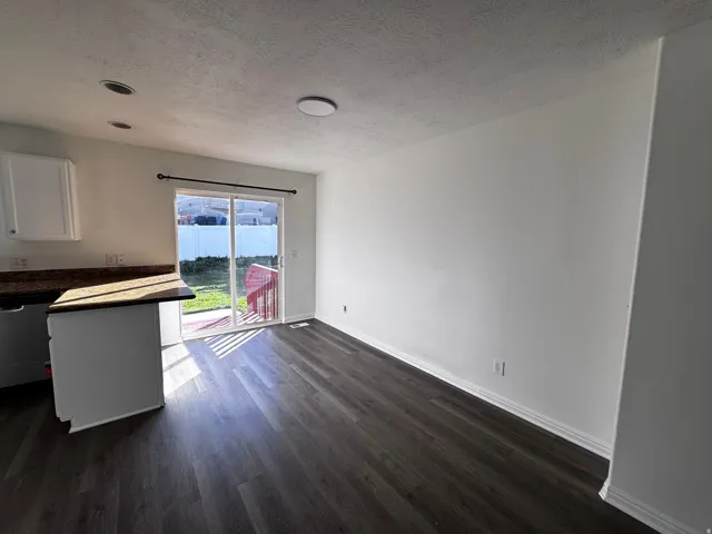 Expansive wood-finish flooring, white cabinetry, granite-style countertops, and sliding glass door