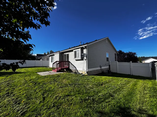 Expansive green lawn, white privacy fencing, rear deck with dark red railing, and light-colored siding