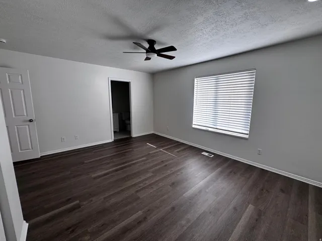 Spacious room featuring wood-finish flooring, a ceiling fan, and a large window with blinds