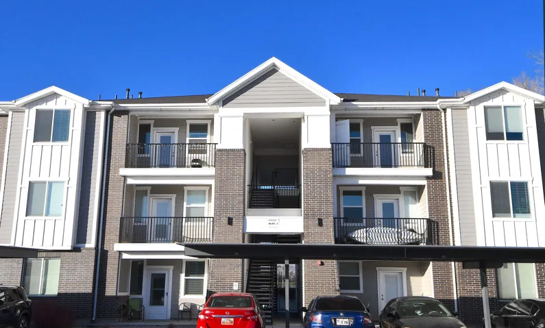 Three-story apartment building with brick and siding exterior, private balconies, and covered parking