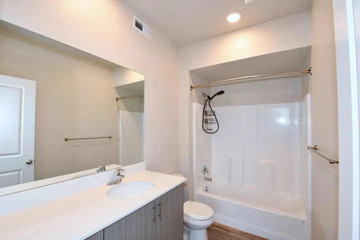 Full-width vanity mirror, single basin vanity, integrated bathtub and shower, recessed lighting, and wood-finish flooring