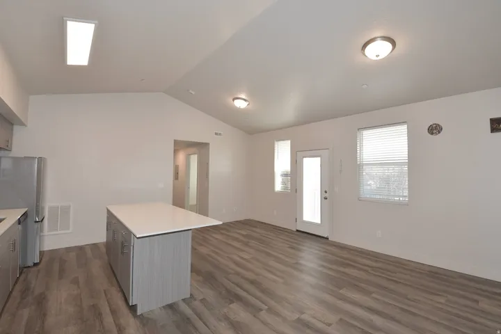 Open concept living area featuring vaulted ceilings, wood-finish flooring, a kitchen island with a light-toned countertop, and stainless steel appliances