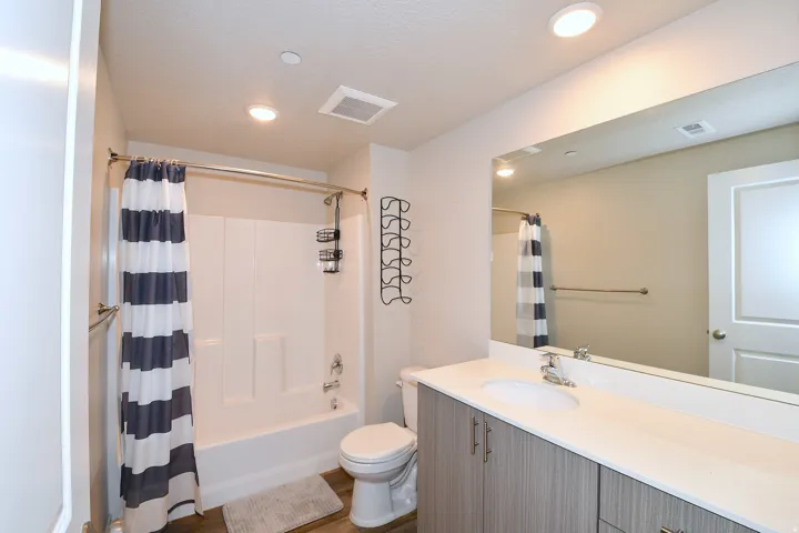 Bathroom featuring a white tub and shower combination, a single vanity with an undermount sink, a large wall-mounted mirror, and wood-finish flooring