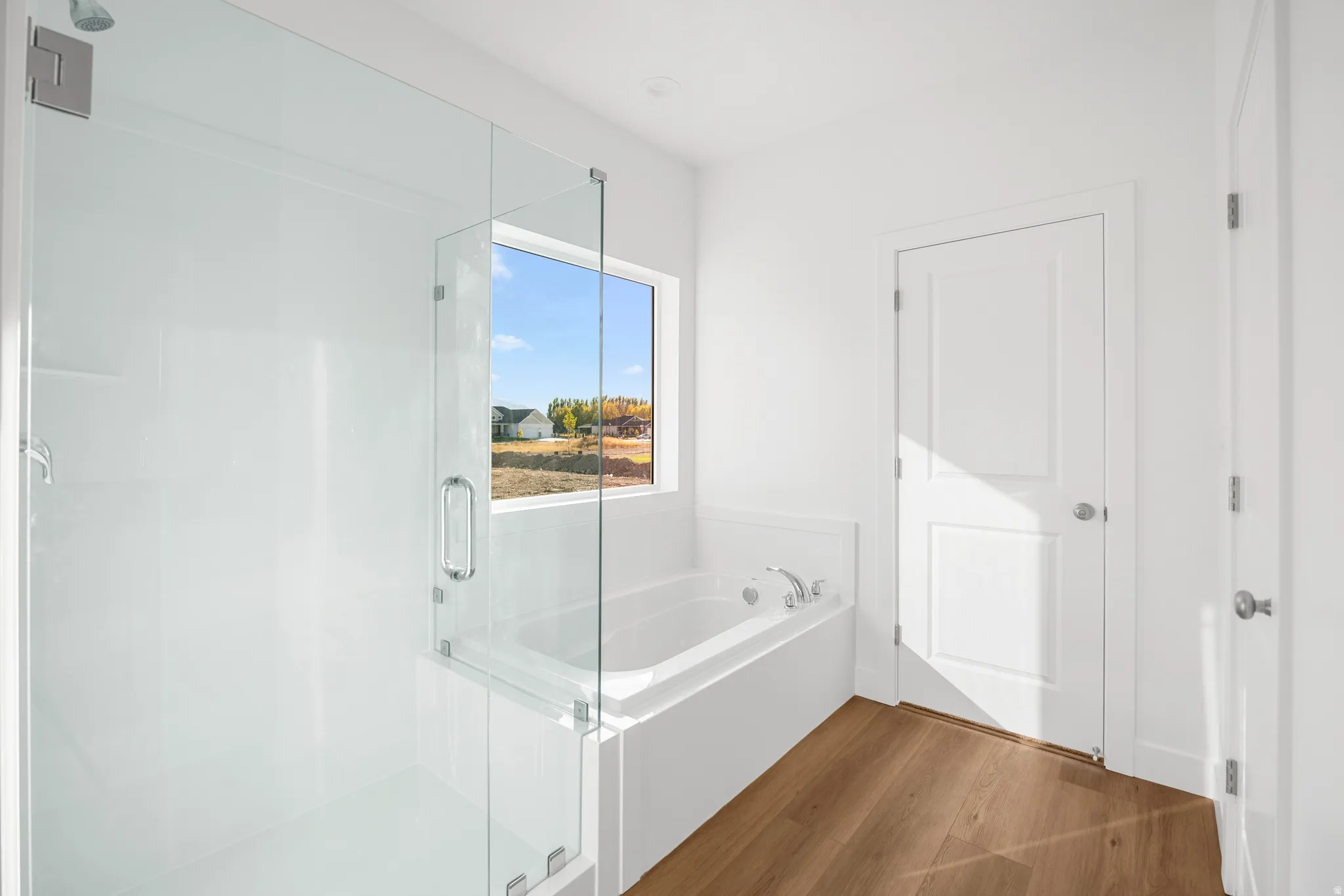 Glass-enclosed shower, soaking tub with window, wood-finish flooring, white paneled doors, and contemporary fixtures
