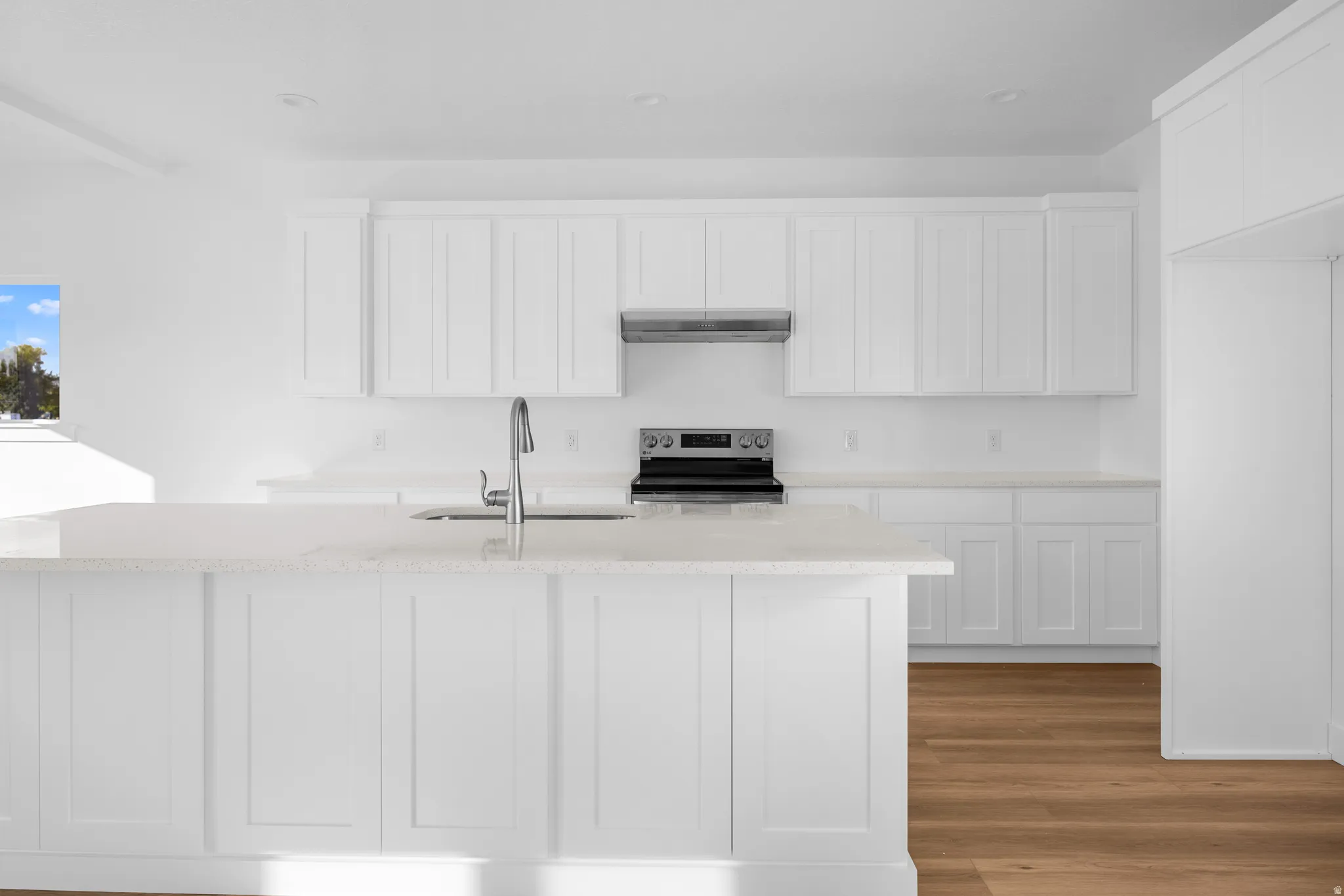 White shaker cabinetry, light-toned countertops, stainless steel range, and wood-finish flooring