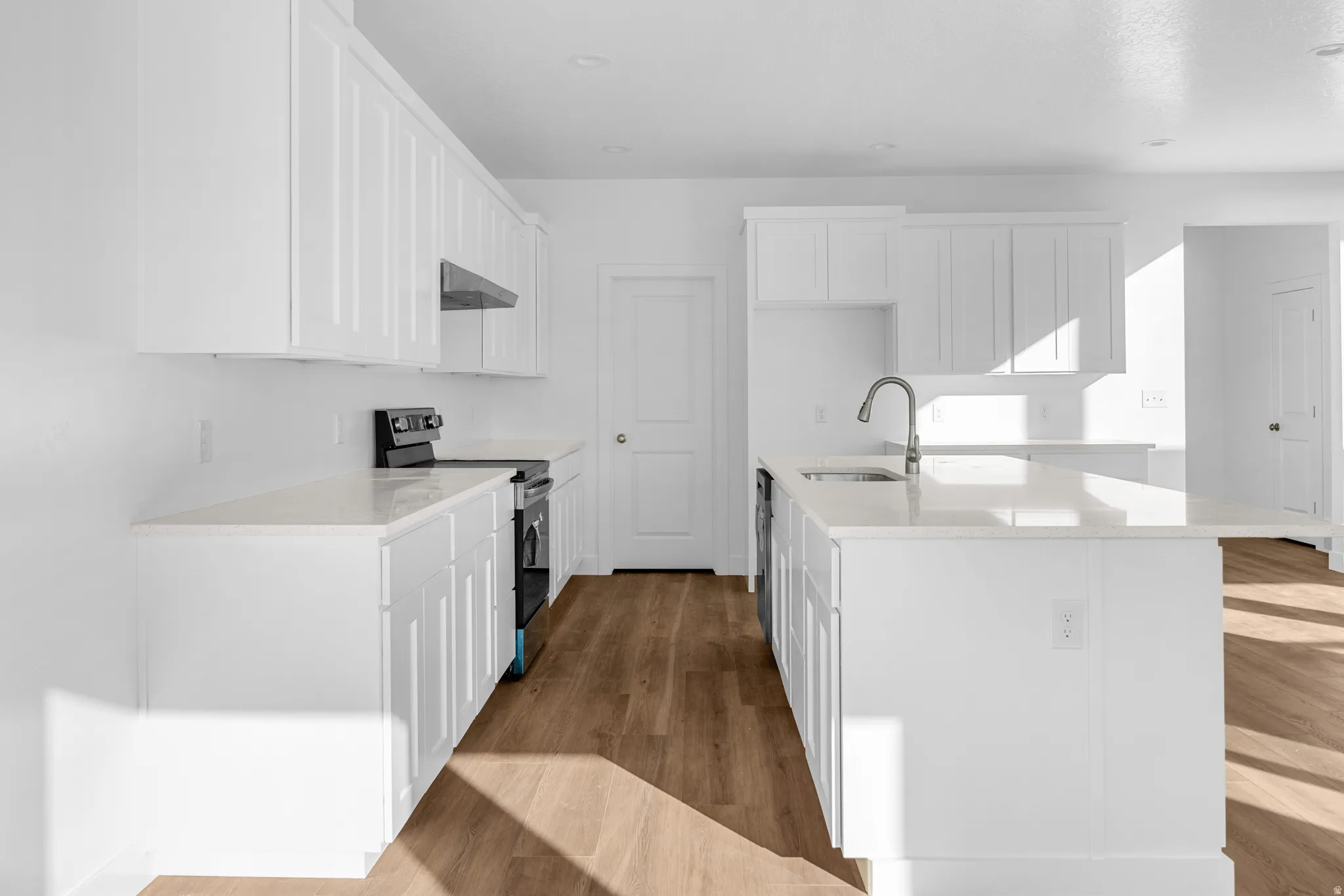 Kitchen featuring white shaker-style cabinetry, light-toned countertops, a stainless steel sink with a gooseneck faucet, and wood-finish flooring