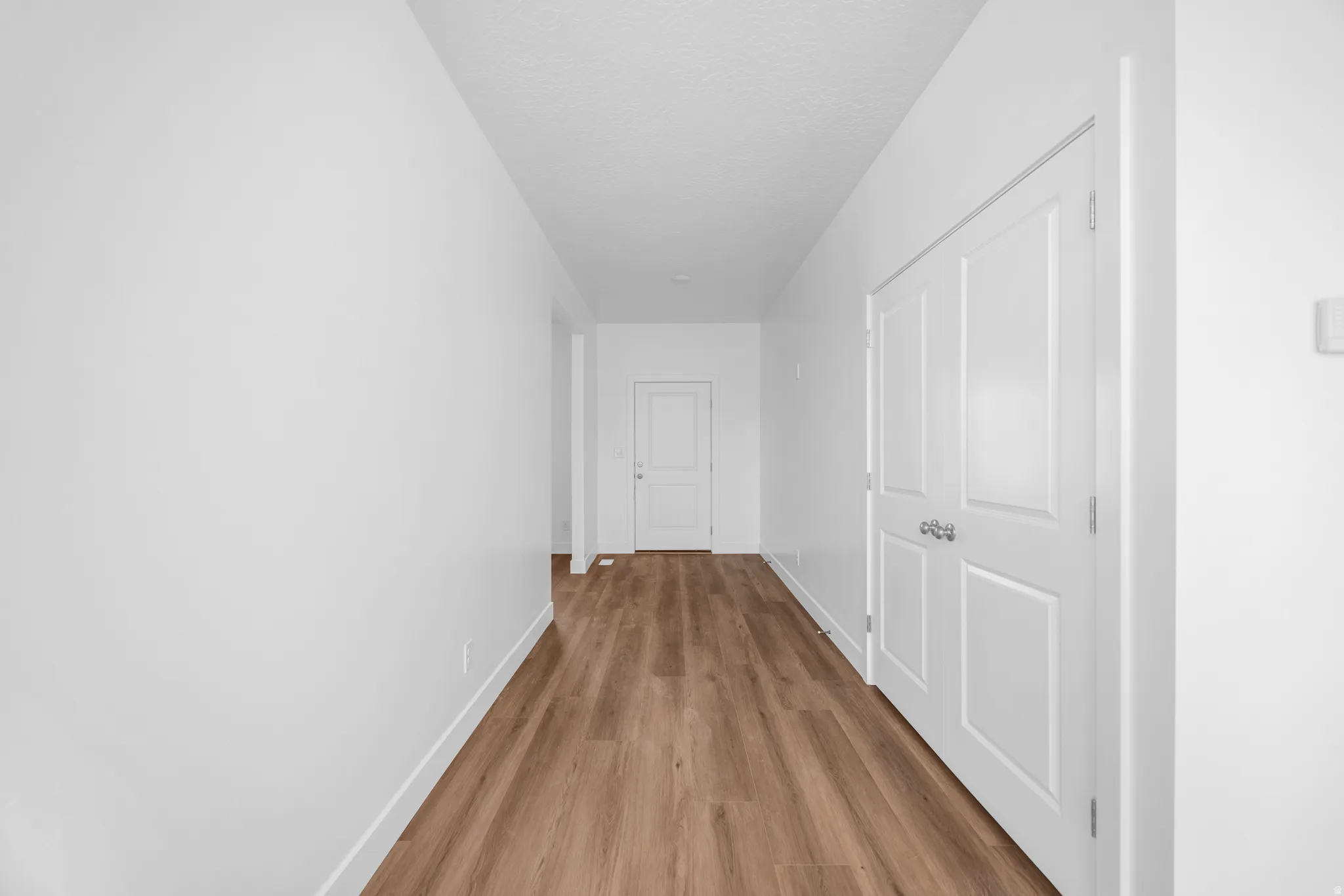 Wood-finish flooring with white baseboards, white walls, white paneled doors, and white ceilings