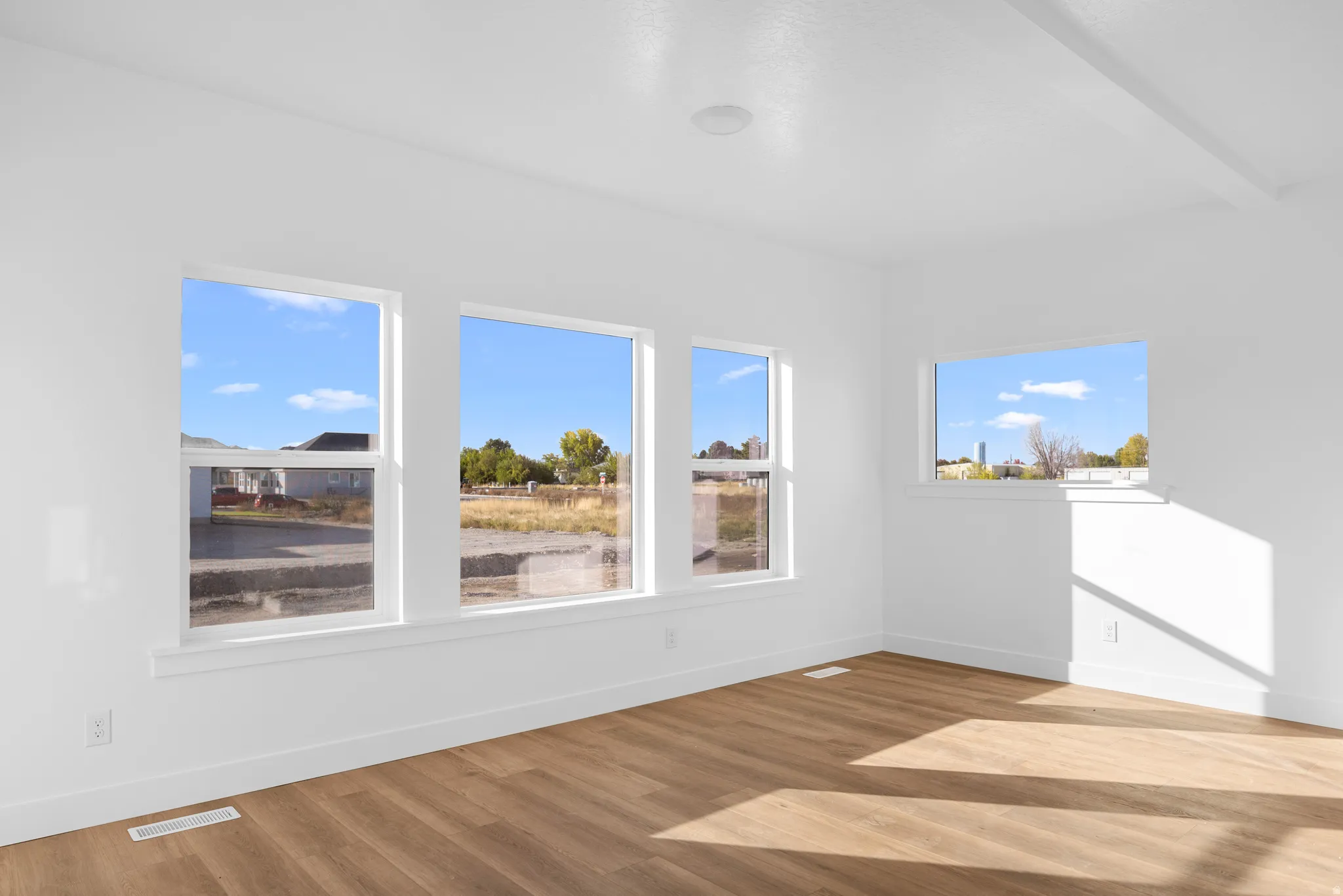 Expansive room featuring multiple windows, wood-finish flooring, and crisp white walls
