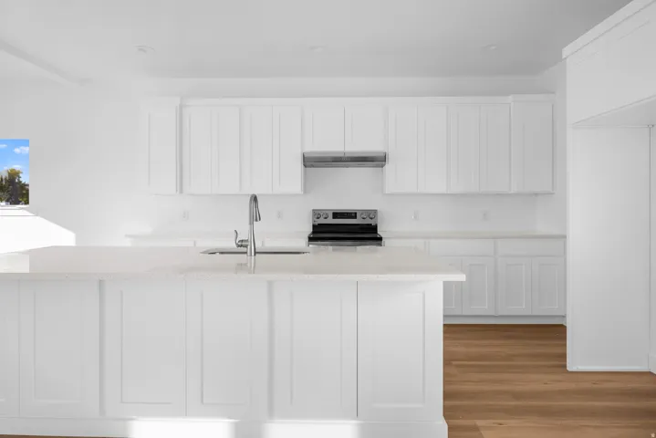 White shaker cabinetry, light-toned countertops, stainless steel range, and wood-finish flooring