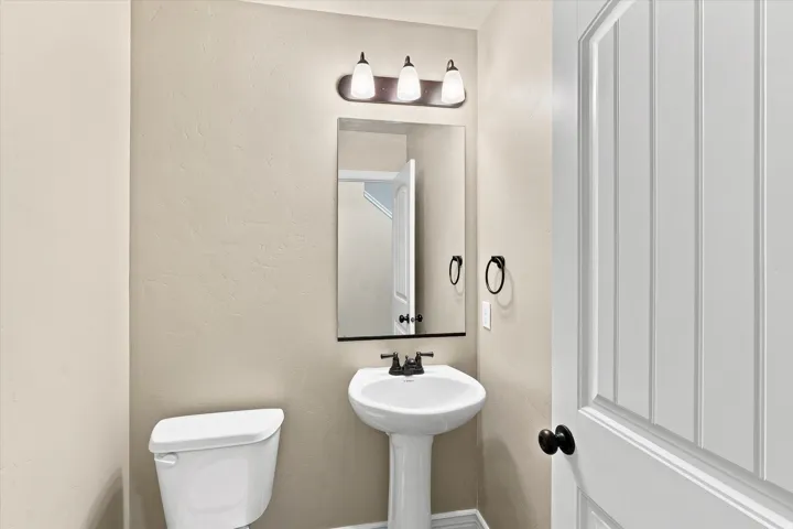 Pedestal sink with black-finish faucet, rectangular mirror, and three-light vanity fixture