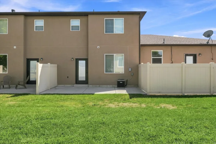 Expansive green lawn with a concrete patio, privacy fencing, and multiple windows across the stucco exterior