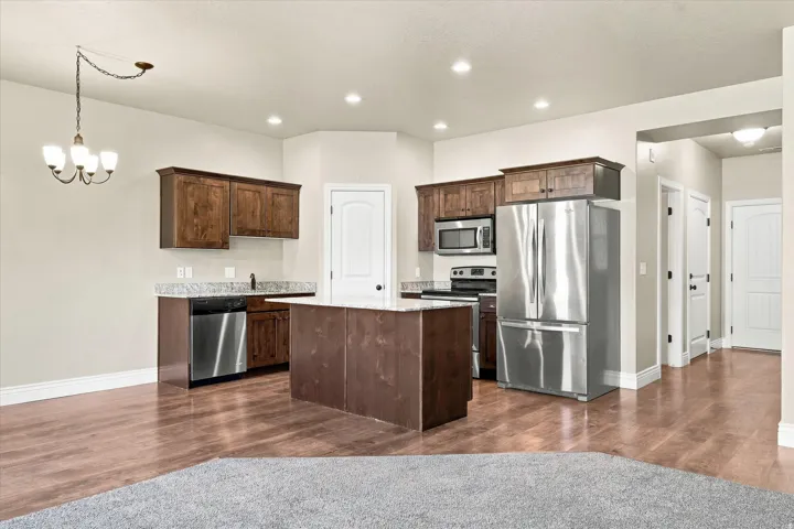 Kitchen featuring wood-finish flooring, recessed lighting, a central island, stainless steel appliances, and dark wood cabinetry with light-toned countertops
