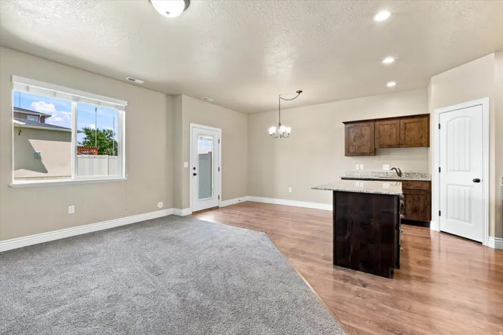 Bright interior with plush carpeting, wood-finish flooring, a kitchen island with granite countertop, and rich wood cabinetry