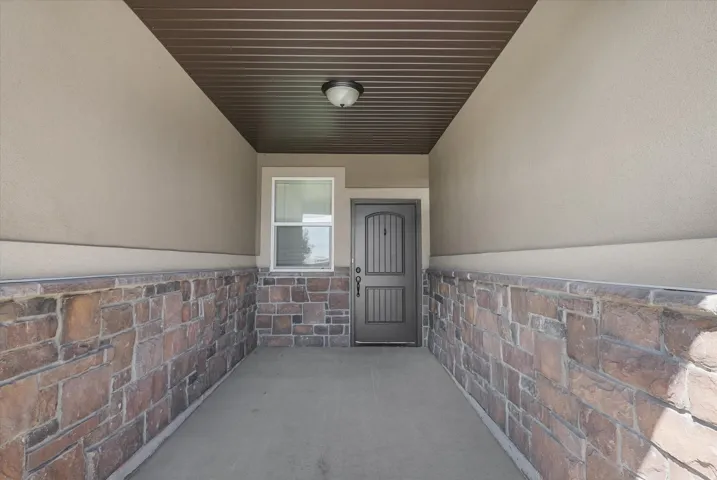 Entryway featuring a stone veneer wainscoting, stucco walls, a dark paneled door, and an overhead light fixture