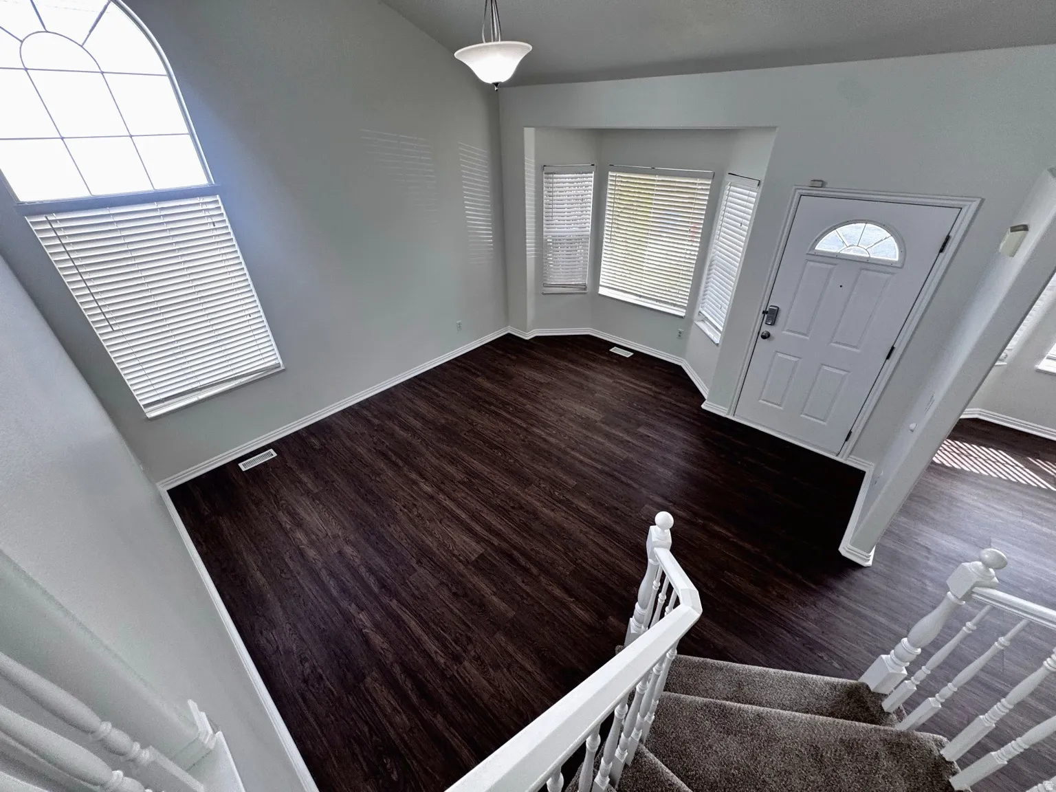 Vaulted ceiling with an arched window, dark wood-finish flooring, and a bay window