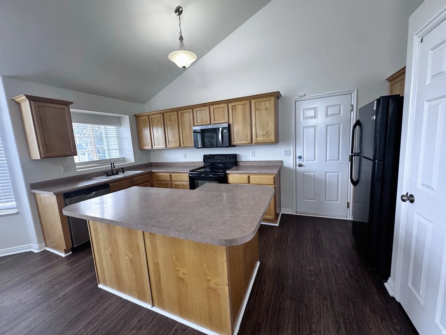 Vaulted ceiling kitchen featuring a center island, wood-finish cabinetry, dark wood-finish flooring, and a stainless-steel dishwasher