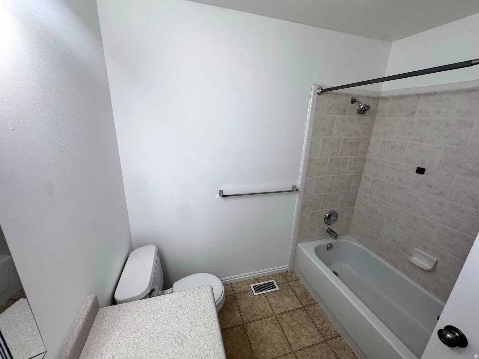 Bathroom featuring a tub/shower combination with tiled surround, a white toilet, and a vanity with a light-toned countertop