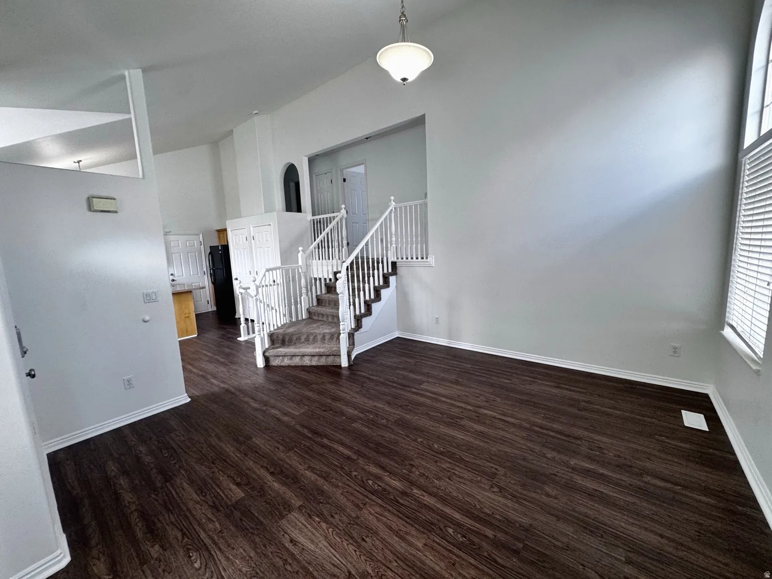 Vaulted ceilings, wood-finish flooring, staircase with carpeted treads, and window with blinds