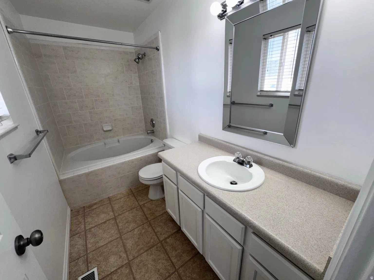 Bathroom featuring a built-in bathtub with tile surround, a single vanity with an integrated sink and light-colored countertop, and a large wall-mounted mirror