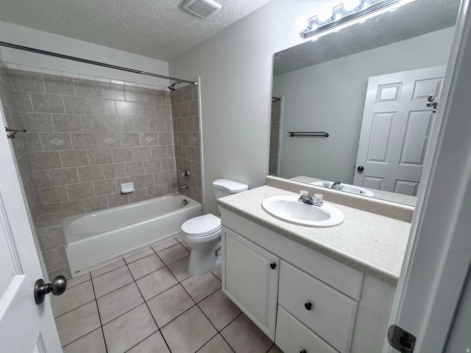 Bathroom featuring a white vanity with an integrated sink, a rectangular mirror, and a shower-over-tub combination with tiled surround