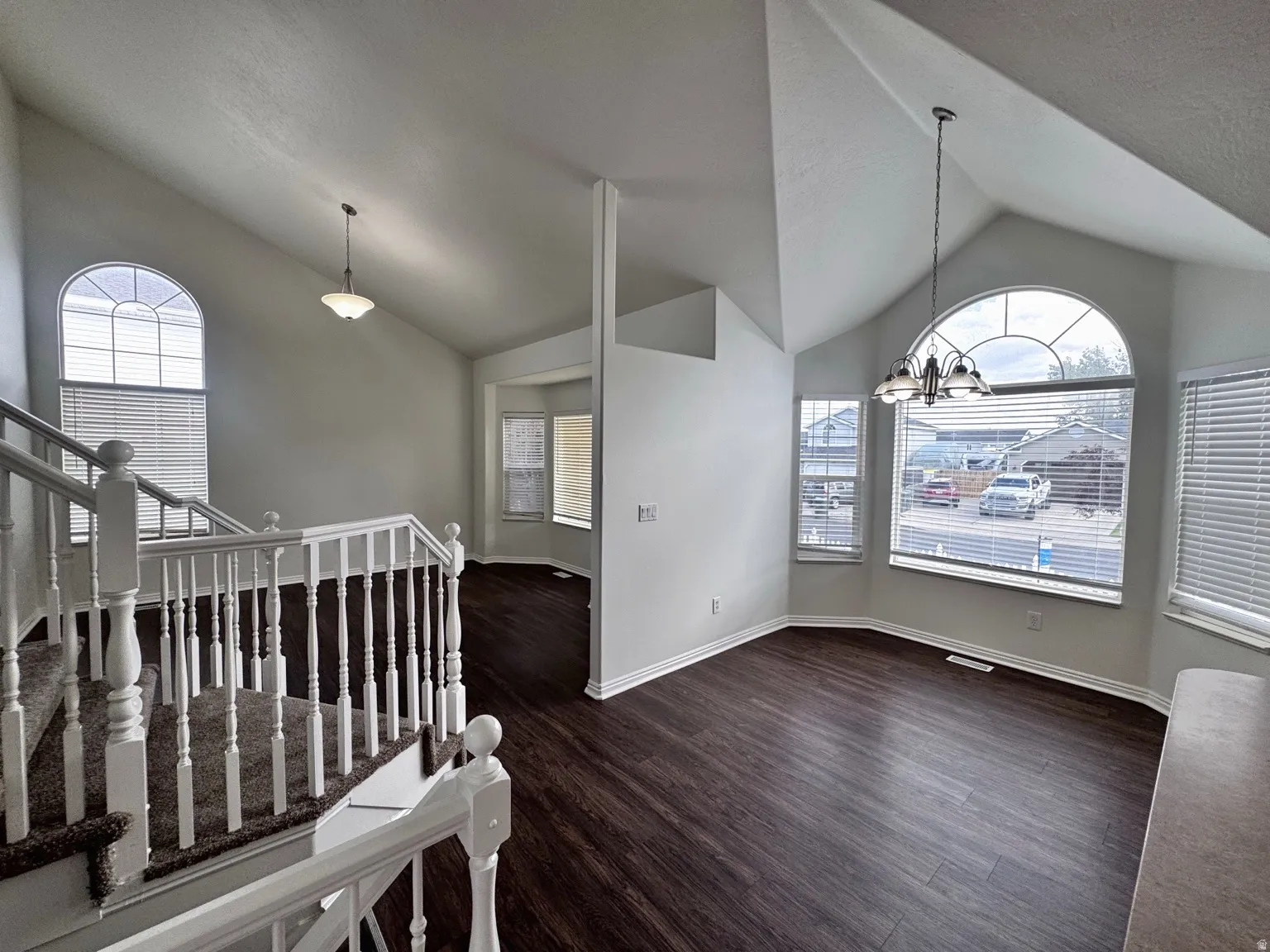 Vaulted ceilings, wood-finish flooring, arched window, staircase with white railing, and bay window