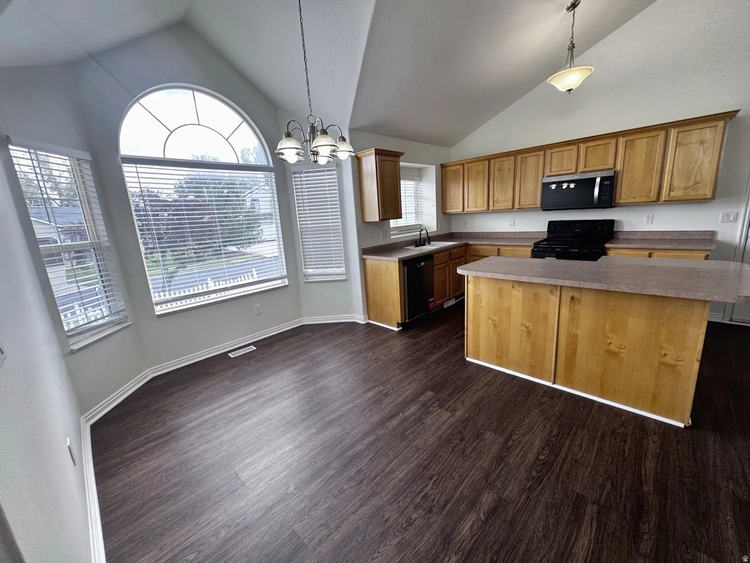 Vaulted ceiling with an arched window, wood-finish flooring, island with a breakfast bar, and wood cabinetry