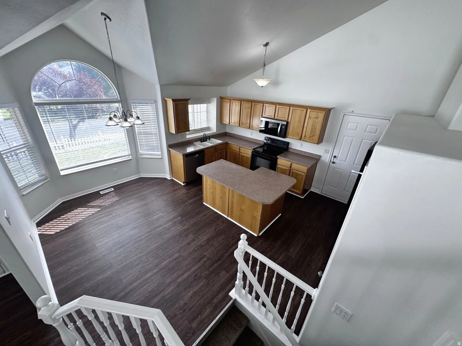Open-concept living space featuring vaulted ceilings, wood-finish flooring, and a kitchen island