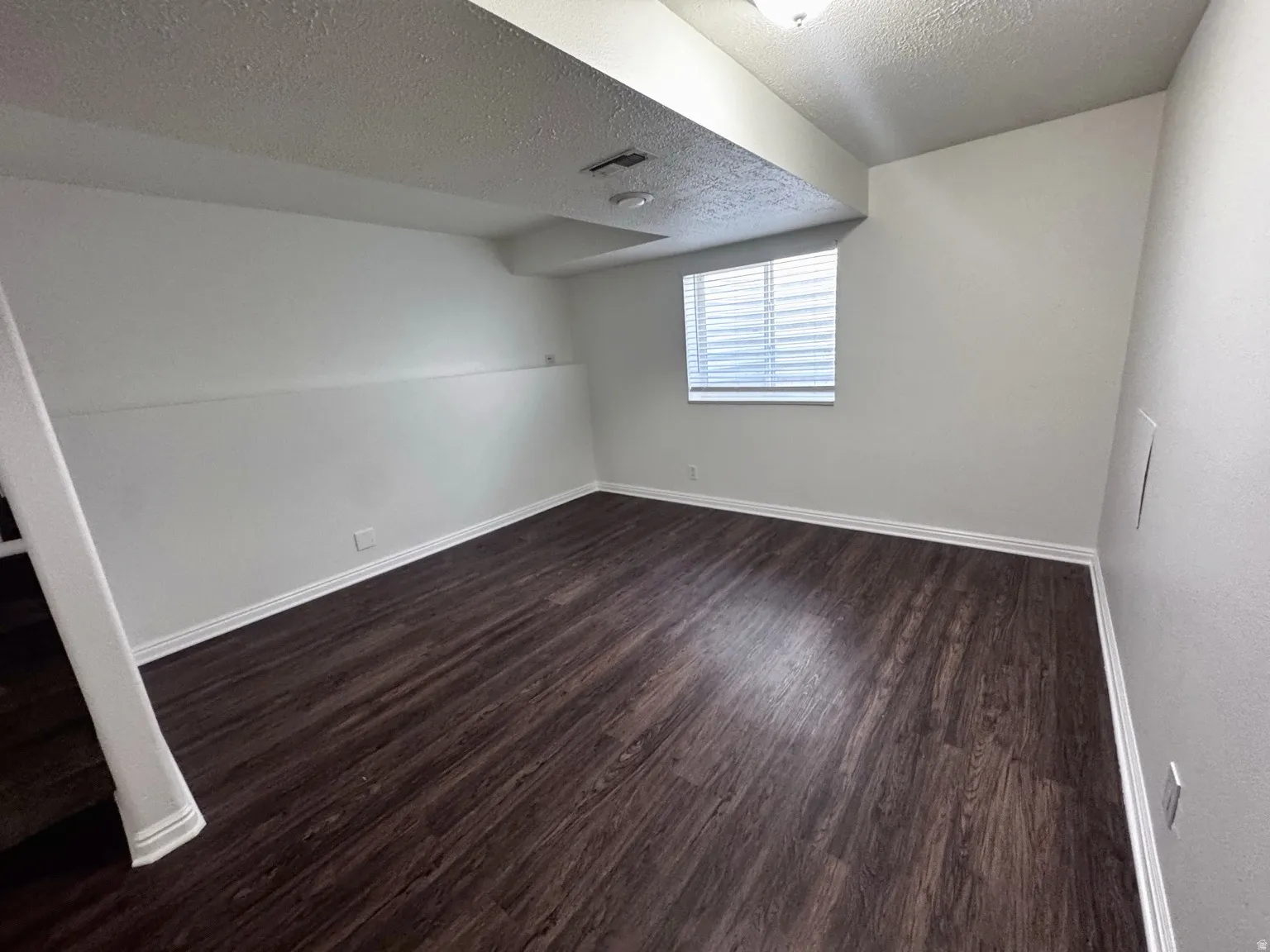 Hardwood-style flooring with white baseboards, white walls, and a window with horizontal blinds