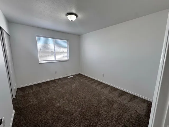 Bright bedroom with expansive carpet flooring, large window with plantation shutters providing natural light, and clean white walls throughout