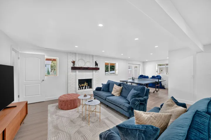 Spacious living area featuring light wood-finish flooring, a white brick fireplace with a dark wood mantel, and recessed ceiling lighting