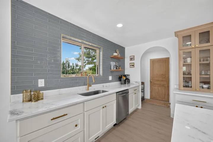 White cabinetry with brass hardware, light-toned wood-finish flooring, and a gray subway tile backsplash