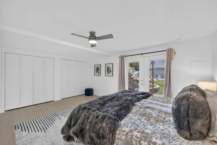 Wood-finish flooring, white bi-fold closet doors, ceiling fan, and French doors leading to exterior