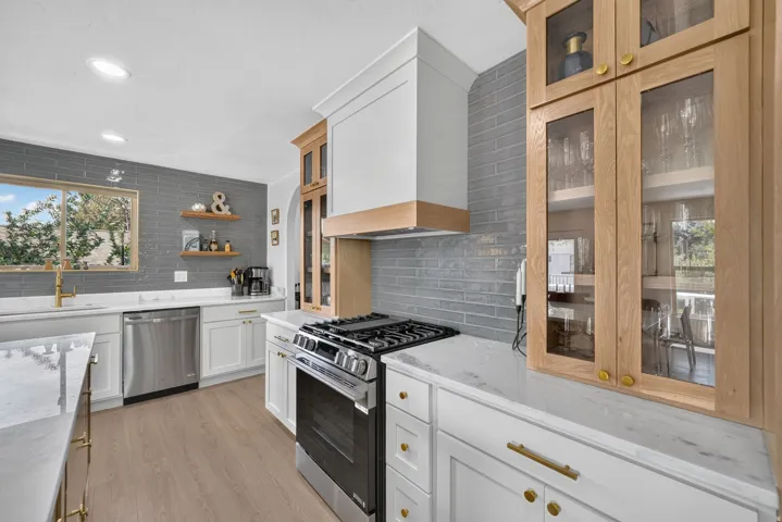 Kitchen featuring wood-finish flooring, white cabinetry with brass hardware, grey subway tile backsplash, white countertops, and stainless steel appliances