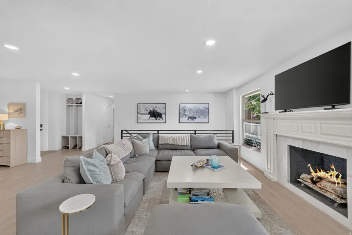 Spacious living area featuring light wood-finish flooring, a white mantel fireplace, recessed lighting, and a built-in hall tree storage unit
