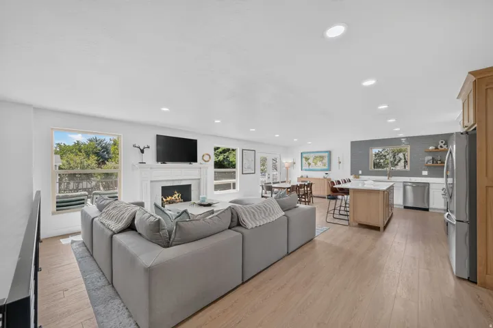 Open-concept living space featuring wood-finish flooring, a white-tiled fireplace, recessed lighting, and a kitchen with stainless steel appliances and an island with seating