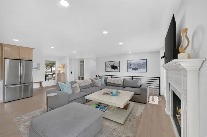 Recessed lighting throughout, light wood-finish flooring, white fireplace with mantle, stainless steel refrigerator, and wood-finish cabinetry