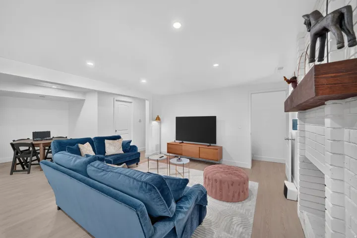 Recessed lighting, light wood-finish flooring, white painted brick fireplace, wood mantel, and a flat panel door