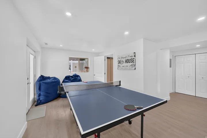 Recessed lighting illuminates this bright room featuring wood-finish flooring, a window, and white interior doors, including double bi-fold closet doors and an exterior access door