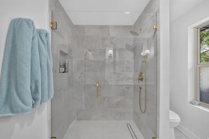 Glass-enclosed shower with full-height tile surround, built-in shower niche, and gold-finish fixtures