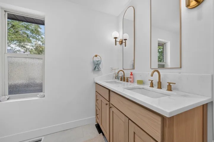 Dual vanity with light wood-finish cabinetry, integrated sinks, and brushed gold fixtures