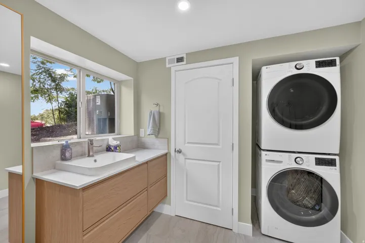 Integrated laundry appliances, wood-finish vanity with drawer storage, white countertop, rectangular vessel sink, and large window