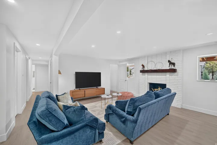 Spacious living area featuring light wood-finish flooring, recessed lighting, and a white brick fireplace with a wood mantel