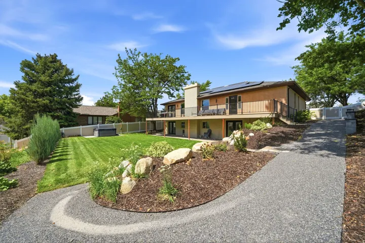 Expansive outdoor living space featuring a spacious lawn, gravel pathway, mature landscaping, upper-level deck, and solar panels