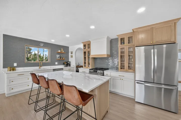 Kitchen featuring a large island with a substantial countertop, wood-finish flooring, white cabinetry, a dark subway tile backsplash, and stainless steel appliances